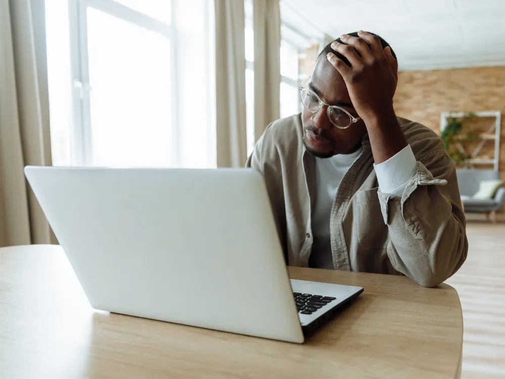 A young man at a laptop, one hand on his head