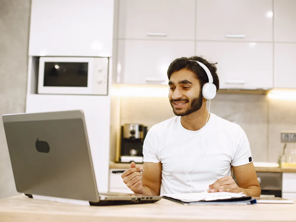A young man with headphones smiling at his laptop