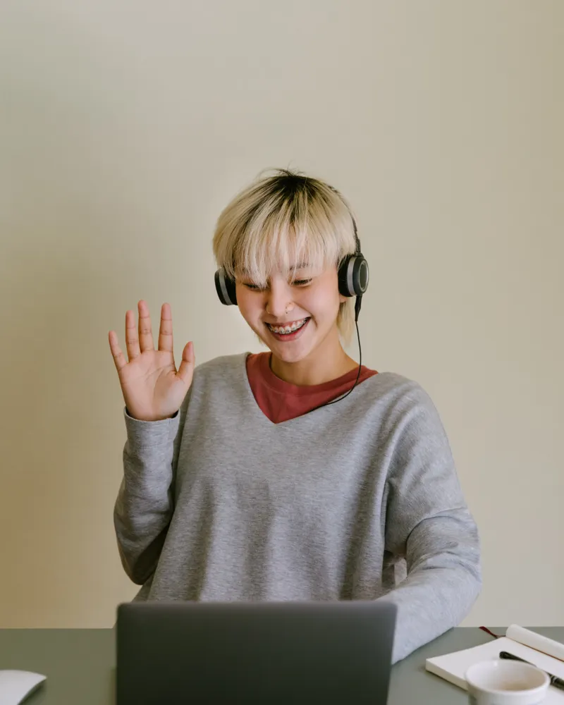 A person in headphones waving at a laptop at the start of a video call