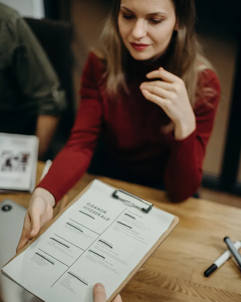 A two-column resume on a clipboard being handed across a desk